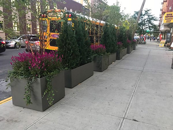 Corten Steel planters filled with green and purple plants line a busy New York street.