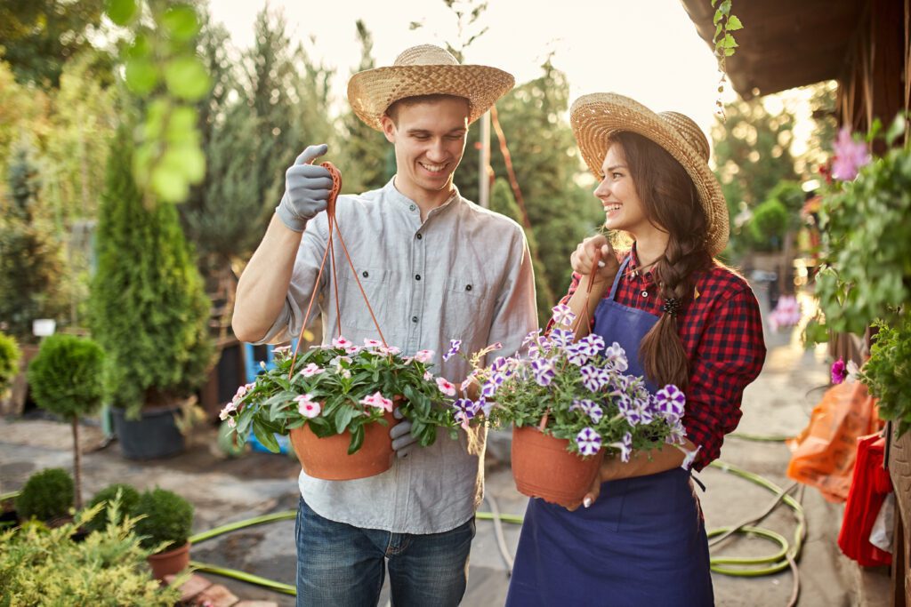 A man and woman holding planters and smiling in a garden.