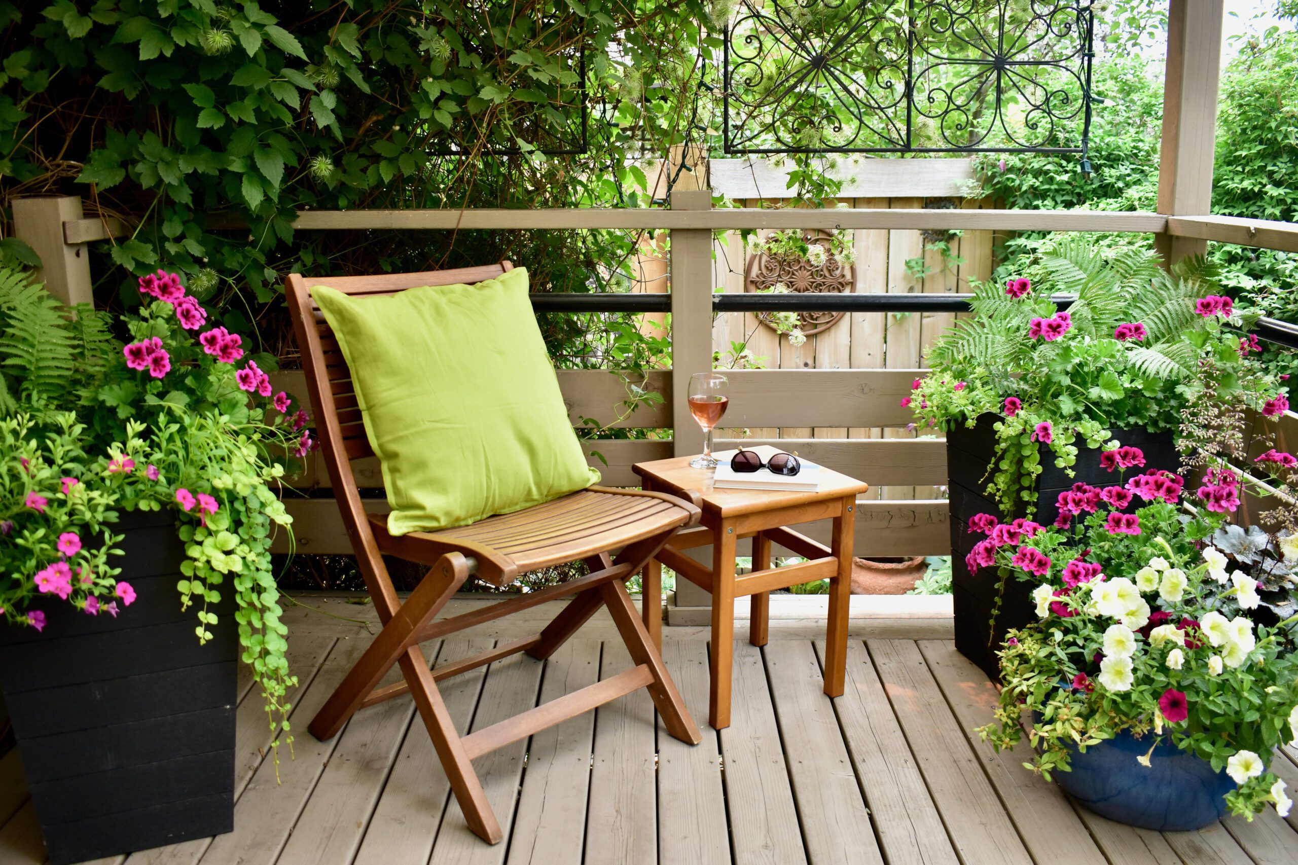 A chair with a pillow and a side table surrounded by planters on a deck.